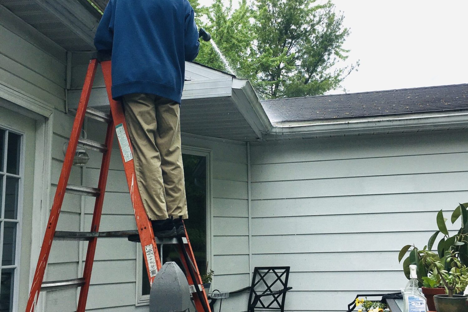 man-on-ladder-cleaning-gutters-on-roof-2023-11-27-05-31-08-utc